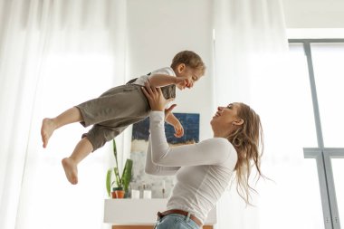 Genç bir anne, küçük oğlunu evde havaya fırlatır, 2 yaşındaki bir çocuk ailesiyle oynar, bir kadın çocuğu yakalar ve birlikte eğlenir.