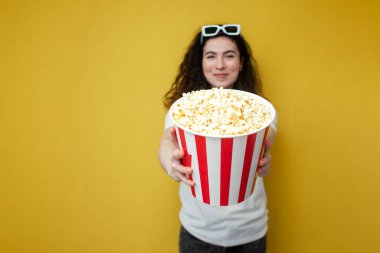 Beyaz tişörtlü genç kıvırcık kız büyük bir kova patlamış mısır gösteriyor, kadın sinemacı reklamları patlamış mısır.