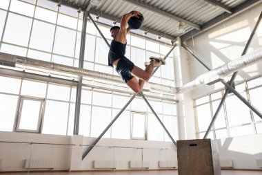 Çapraz formda antrenman yapan sporcu atlıyor ve tıp topunu salona atıyor. Güçlü adam topla spor yapıyor ve zıplama egzersizi yapıyor.