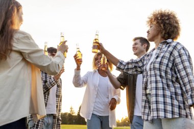 Bir grup çok ırklı genç ellerinde bira şişeleri ve açık hava partisinde konuşuyorlar. Afrikalı Amerikalı kız ve erkek arkadaşları parkta gülüyor ve içki içiyorlar.