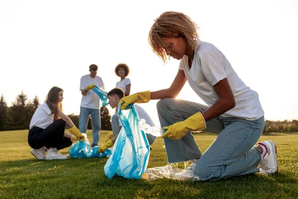Eldivenli ve çöp torbalarıyla parktaki plastik ve çöpleri kaldıran bir grup çok ırklı insan, gönüllülerden oluşan bir ekip plastik şişeleri toplayıp çalışıyor, insanlar çevreye, yeşil gezegene önem veriyor.