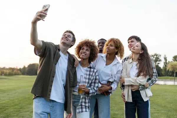 group of multiracial young people take selfies on smartphone and take pictures in the park, interracial students communicate via video communication online outdoors