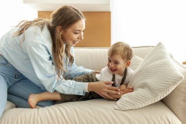 Genç anne, küçük oğlunu kanepeye yatırır ve üstünü battaniyeyle örter. 2 yaşındaki çocuk, ailesiyle birlikte kahkahalarla oynar. Kadın büyür ve çocuğa bakar.