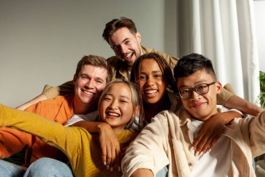 Kameraya gülümseyen ve selfie çeken çok ırklı genç arkadaşlar, Asyalı, Afrikalı, Amerikalı ve Avrupalı öğrenciler kucaklaşıp fotoğraf çekiyorlar.