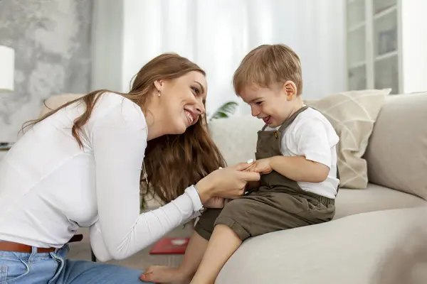 stock image young mother holds the hands of her little son and smiles, 2-year-old boy sits on the sofa with his parent, woman raises and takes care of the child