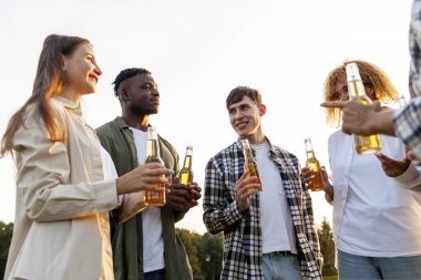 Bir grup çok ırklı genç ellerinde bira şişeleri ve açık hava partisinde konuşuyorlar. Afrikalı Amerikalı kız ve erkek arkadaşları parkta gülüyor ve içki içiyorlar.