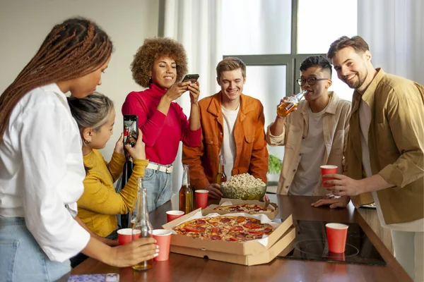 multiracial group of young people at house party ordered pizza and beer and photographed food on phone, students of different ethnicities at house party drink alcohol and eat fast food and have fun