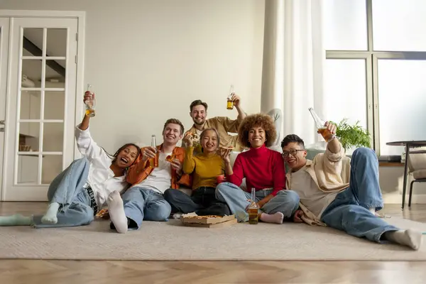 stock image multiracial group of people at house party eating pizza and drinking beer and having fun with friends, students drinking alcohol and eating fast food and watching TV and celebrating