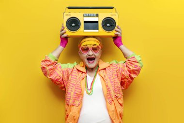 Spor kasetçaları ve hippi kıyafetleriyle müzik dinleyen ve sarı izole edilmiş arka planda şarkı söyleyen yaşlı, şık giyinmiş, piknik çalan yaşlı bir kadın partilerde çığlıklar atıyor.