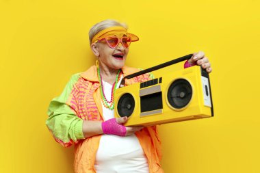 Spor kasetçaları ve hippi kıyafetleriyle müzik dinleyen ve sarı izole edilmiş arka planda şarkı söyleyen yaşlı, şık giyinmiş, piknik çalan yaşlı bir kadın partilerde çığlıklar atıyor.