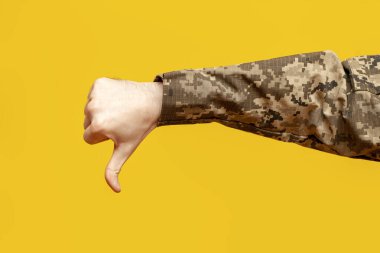 Ukrayna ordusunun kamuflaj piksel üniformalı bir erkek askerinin eli sarı izole bir arka plan, kötü bir başarısızlık ve reddetme jesti, yakın plan