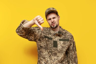 Kamuflaj piksel üniformalı genç Ukraynalı erkek asker, sarı izole bir geçmişe karşı hoşnutsuzluk ve hoşnutsuzluk gösteriyor.