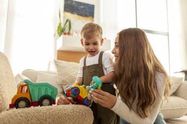 Genç anne ve küçük oğlu evde oyuncaklarla oynuyorlar, 2 yaşındaki çocuk oyuncak araba tutuyor ve ailesiyle eğleniyor, kadın çocuğa bakıyor ve büyütüyor.
