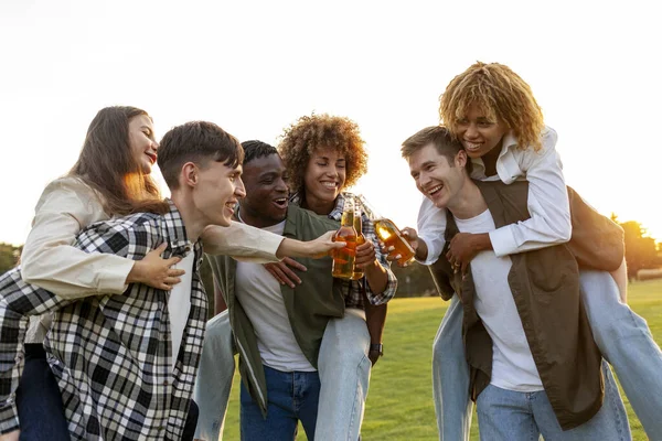 three couples of young multiracial people drinking beer and celebrating toast at party in the park, interracial group of friends drinking alcohol and having fun outdoors