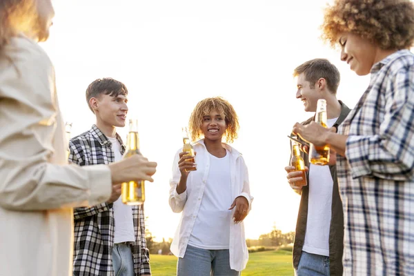 group of multiracial friends at party chatting and drinking beer outdoors, african american women and men talking and laughing and holding bottle, group of people having fun