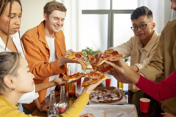 multiracial group of young people at a house party ordered pizza and beer, students of different ethnicities at a house party drink alcohol and eat fast food and have fun