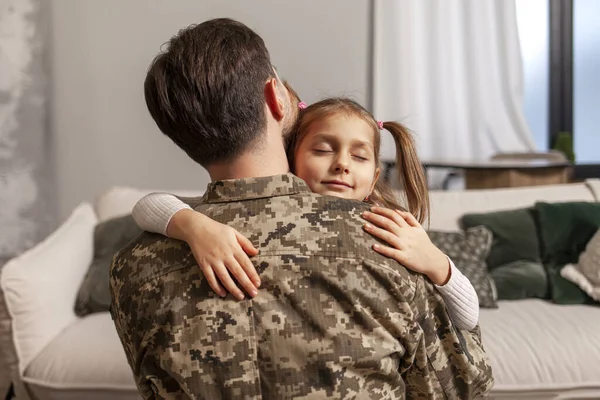 young Ukrainian soldier in a camouflage uniform hugs a child at home and says goodbye, a little girl hugs and greets a military dad, a happy child meets his father from the army