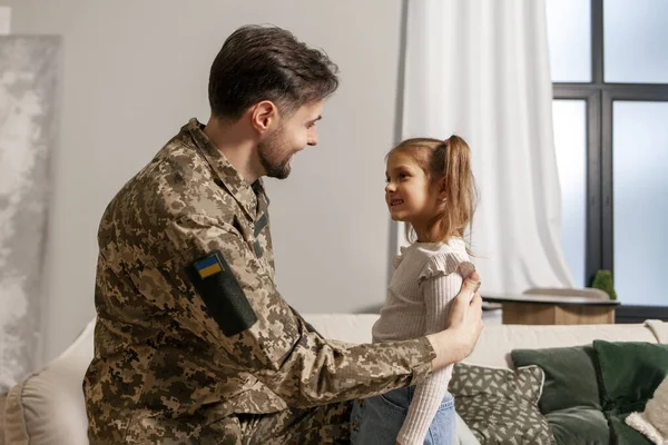 young Ukrainian soldier in a camouflage uniform hugs a child at home and says goodbye, a little girl hugs and greets a military dad, a happy child meets his father from the army