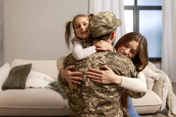 young soldier of the Ukrainian army in a camouflage uniform returned home to his family, a military dad hugs his little daughter and wife at home