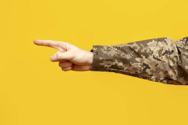 Kamuflaj üniforması giymiş bir Ukraynalı askerin eli sarı izole edilmiş bir arka plana parmak basar ve işaret eder. Bir askerin eli bir numarayı gösterir ve seçer.