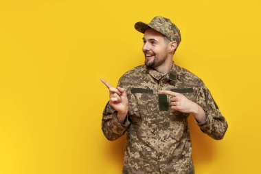 Ukraynalı asker, kamuflaj üniformalı asker ellerini sarı izole bir arka planda boş bir alana koyuyor. Ukraynalı askeri öğrenci uzay kopyaları ve reklamları gösteriyor.