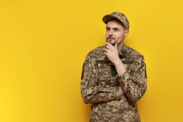 pensive ukrainian army soldier in camouflage uniform pixel plans and thinks on a yellow isolated background, ukrainian military cadet dreams and imagines