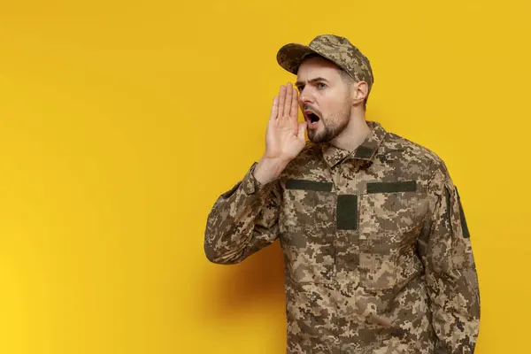 Ukrainian army soldier in pixel camouflage uniform announces information and shouts on a yellow isolated background, Ukrainian military cadet says