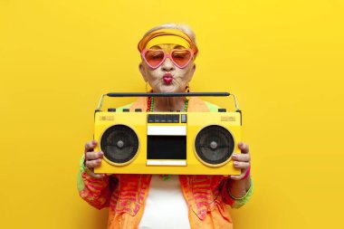 Hippi kıyafetleri içinde, müzik dinleyen, sarı izole edilmiş bir arka planda öpüşen yaşlı ve havalı bir kadın partide dans edip eğleniyor.