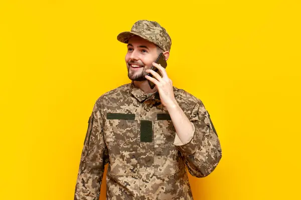 Ukrainian army soldier in a pixel camouflage uniform talks on the phone on a yellow isolated background, a Ukrainian military cadet communicates via mobile communication