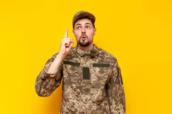 I have an idea. young Ukrainian army soldier in camouflage pixel uniform pointing with finger up and surprised on yellow isolated background, Ukrainian military cadet came up with a solution