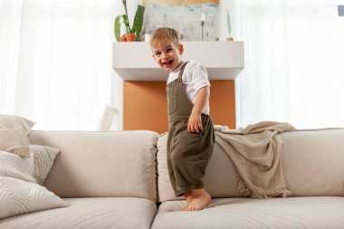 Küçük çocuk 2 yaşında, evdeki yumuşak rahat koltukta duruyor ve gülüyor, mutlu çocuk gülüşleri, boşluğu kopyalıyor.