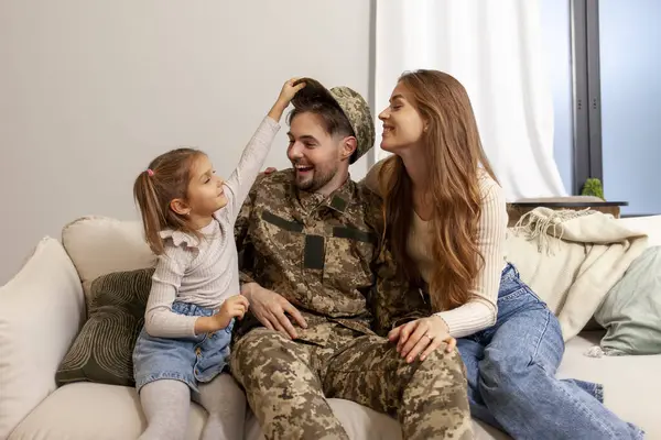 happy soldier of Ukrainian army in camouflage uniform returned home to his family, military dad meets and hugs his wife and daughter at home, concept of mobilization in Ukraine