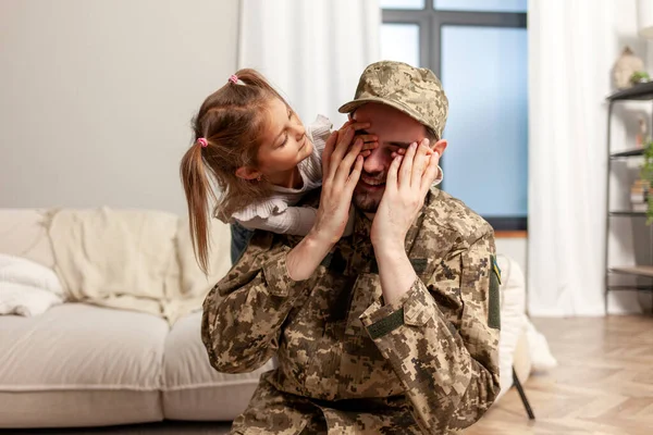 happy soldier of Ukrainian army in camouflage uniform returned home to his family, child closes his eyes to his military dad and makes surprise at home