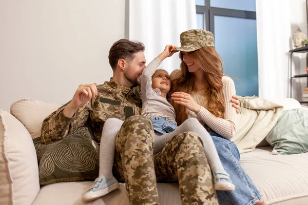 happy soldier of Ukrainian army in camouflage uniform returned home to his family, military dad meets and hugs his wife and daughter at home, concept of mobilization in Ukraine