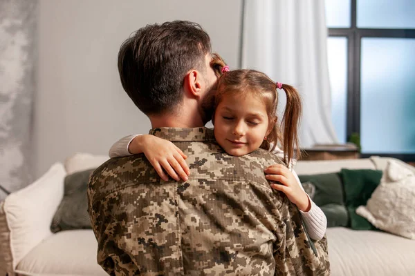 military man of the Ukrainian army in camouflage uniform returned home and hugs his daughter, soldier goes to war and says goodbye to his child, the concept of mobilization in Ukraine