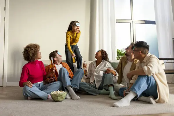 multiracial group of young friends playing charades drinking beer and having fun at home, students sitting on the sofa and pretending to be different animals and drinking alcohol together in the room