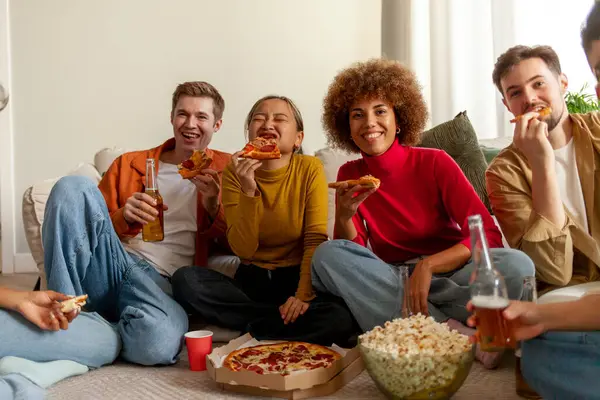 multiracial group of young people at house party eating pizza and drinking beer and having fun with friends, students of different ethnicities at a house party drinking alcohol and eating fast food
