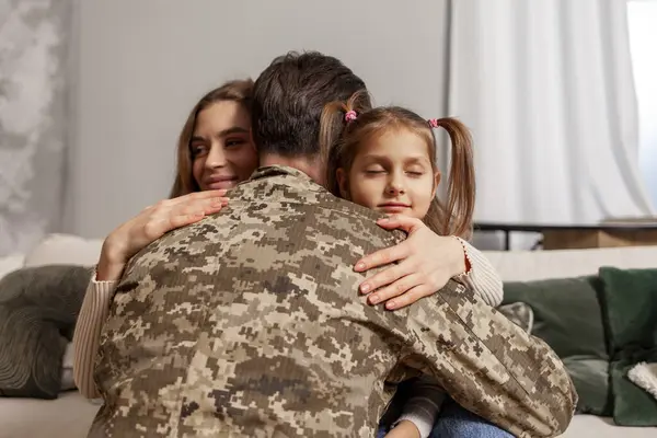 military man of the Ukrainian army in camouflage uniform returned home and hugs his family, soldier goes to war and says goodbye to his daughter and wife, the concept of mobilization in Ukraine