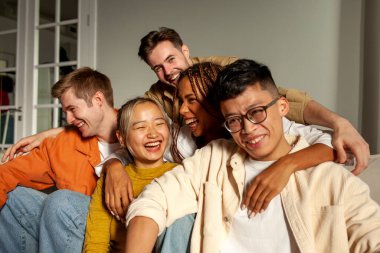 Kameraya gülümseyen ve selfie çeken çok ırklı genç arkadaşlar, Asyalı, Afrikalı, Amerikalı ve Avrupalı öğrenciler kucaklaşıp fotoğraf çekiyorlar.