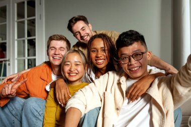 Kameraya gülümseyen ve selfie çeken çok ırklı genç arkadaşlar, Asyalı, Afrikalı, Amerikalı ve Avrupalı öğrenciler kucaklaşıp fotoğraf çekiyorlar.