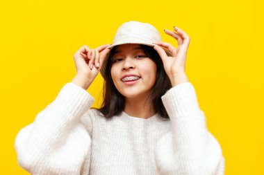 Diş teli takan genç Asyalı kadın sarı izole edilmiş arka planda panama şapkasını takıyor Koreli kız gülümsüyor ve şapkasının güneşliğiyle yüzünü örtüyor.