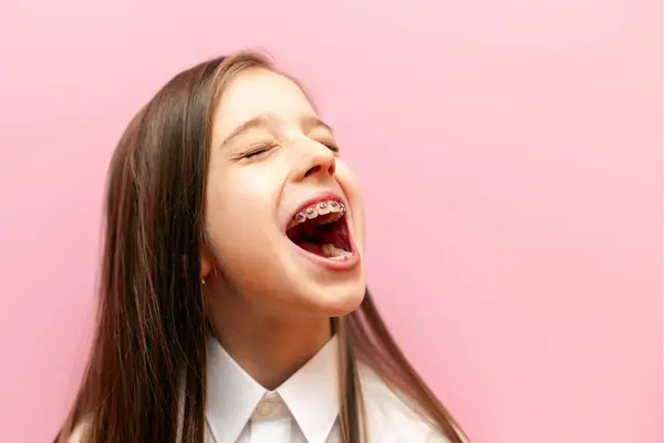 Diş telleri yüksek sesle bağıran ve pembe izole bir arka planda anons yapan ağzı açık bir çocuk konuşuyor.