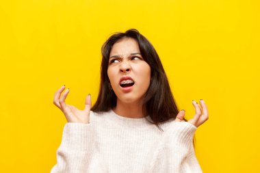 Asyalı sinirli genç bir kız sarı izole edilmiş arka planda öfke çığlıkları atıyor. Stres ve depresyondaki tatminsiz Koreli kız ellerini kaldırıyor.