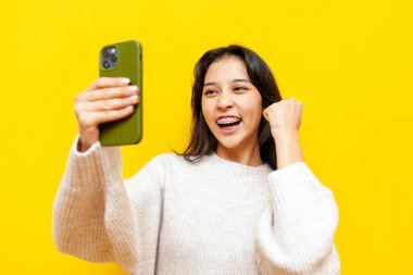 Akıllı telefon kullanan ve sarı izole edilmiş arka planda kazanan Asyalı genç bayan, Koreli kız başarıyı kutluyor ve internette iyi şanslar.