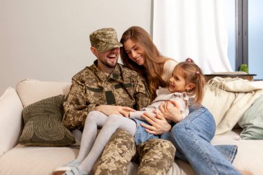 Kamuflaj üniformalı Ukraynalı asker evine, ailesine döndü, askeri öğrenci karısı ve kızıyla kanepede oturdu ve gülümsedi.