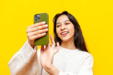 Telleri akıllı telefon kullanan ve sarı izole edilmiş arka planda interneti seçen Koreli genç mutlu Asyalı kadın, telefonda yazan ve gülümseyen Koreli kız.