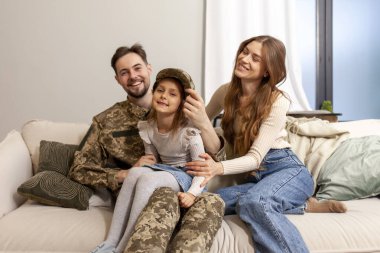 Kamuflaj üniformalı Ukraynalı asker evine, ailesine döndü, askeri öğrenci karısı ve kızıyla kanepede oturdu ve gülümsedi.