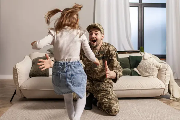 happy Ukrainian army soldier in camouflage uniform returned home and meets his daughter, the child runs to his military dad and hugs the veteran at home