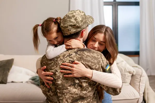 military man of the Ukrainian army in camouflage uniform returned home and hugs his family, soldier goes to war and says goodbye to his daughter and wife, the concept of mobilization in Ukraine