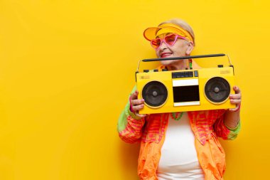 Hippi kıyafetleri içinde, müzik dinleyen, sarı izole edilmiş bir arka planda öpüşen yaşlı ve havalı bir kadın partide dans edip eğleniyor.